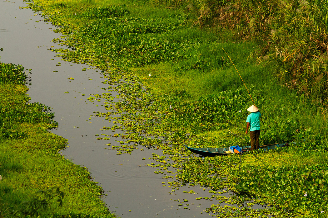 A fisherman stands in his boat in a canal in Kien Giang Province, Vietnam