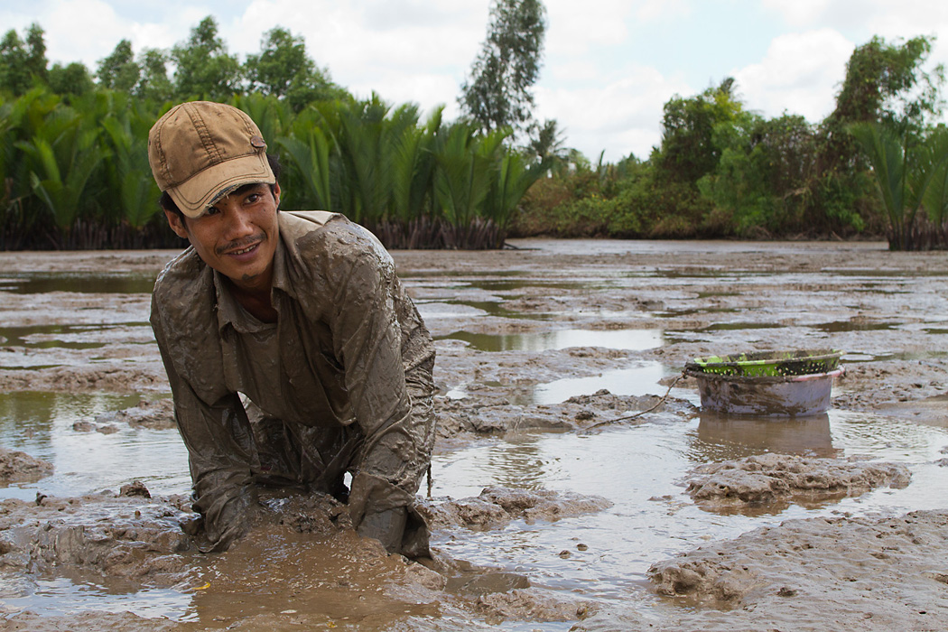 A man digs for eels in the muddy river sediment near Ca Mau in the Mekong Delta 