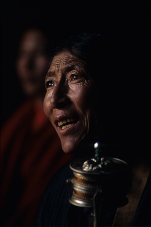 A pilgrim, holding a prayer wheel, watches the monks at the Jokhang monastery